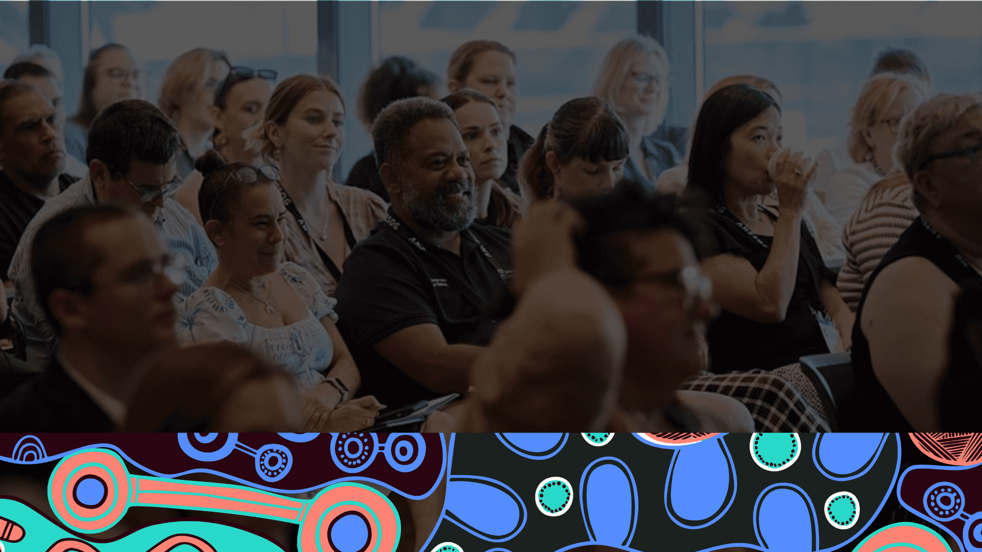 Audience attentively listening at a conference, with colorful abstract patterns at the bottom of the image.