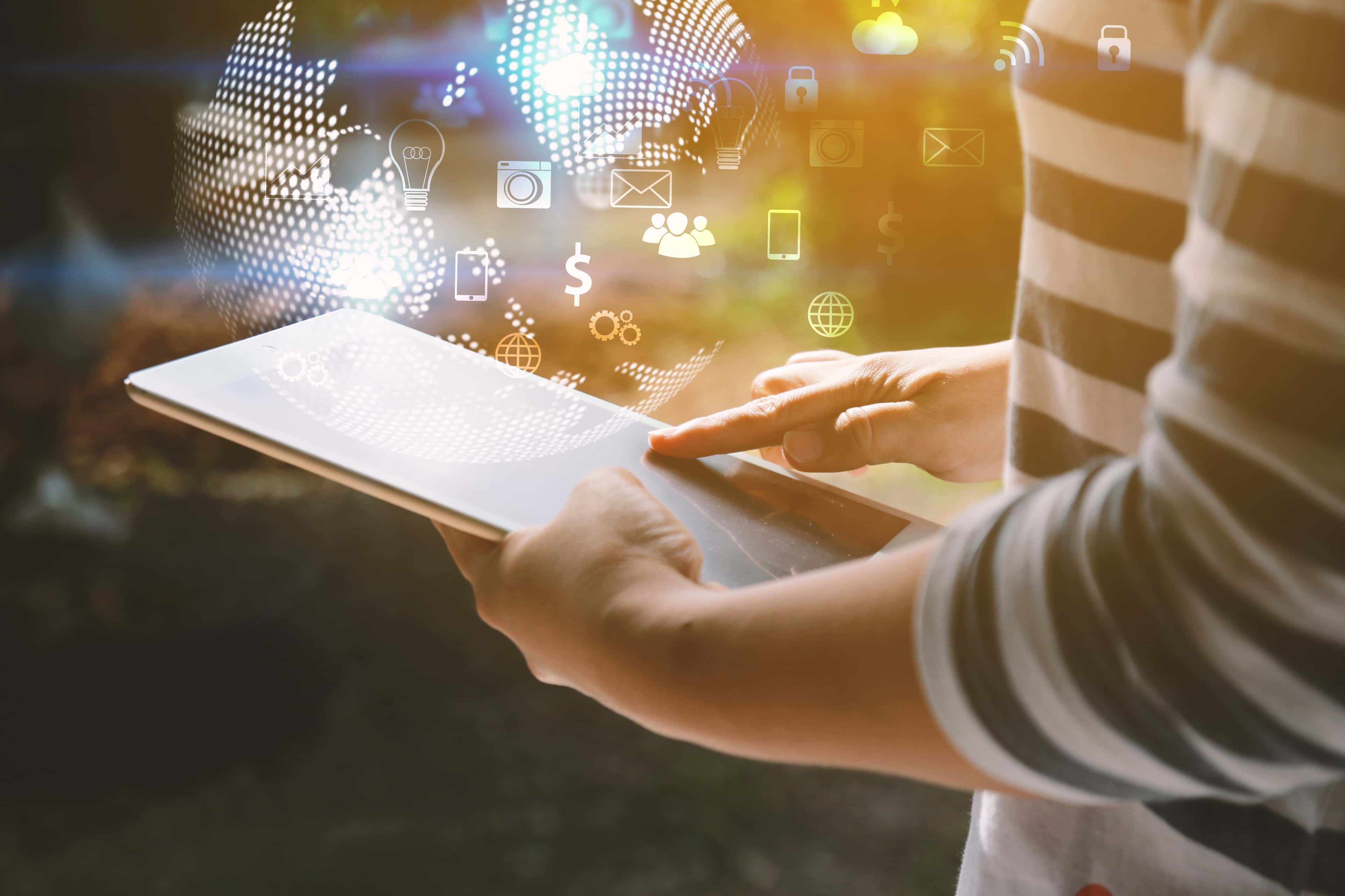 Person using a tablet outdoors with digital icons of communication and technology floating above the screen.
