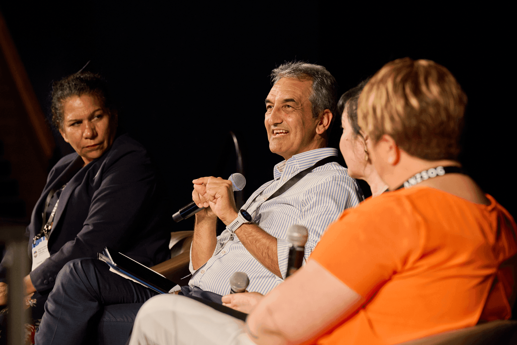 A panel of four people engaging in discussion on stage, with one person speaking into a microphone.