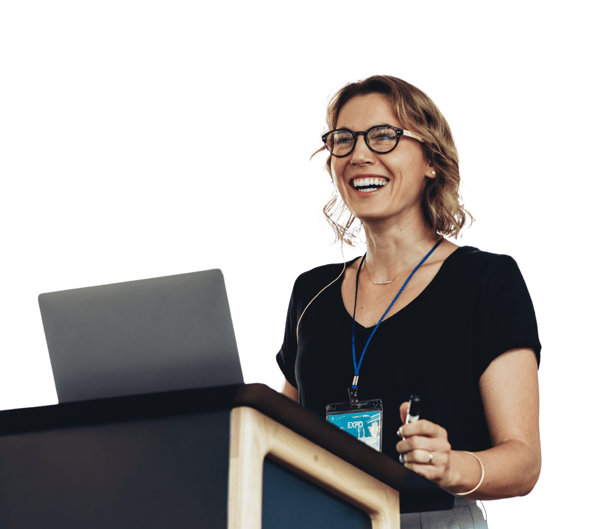 Smiling woman with glasses and a conference badge presenting at a podium with a laptop, wearing a black top.