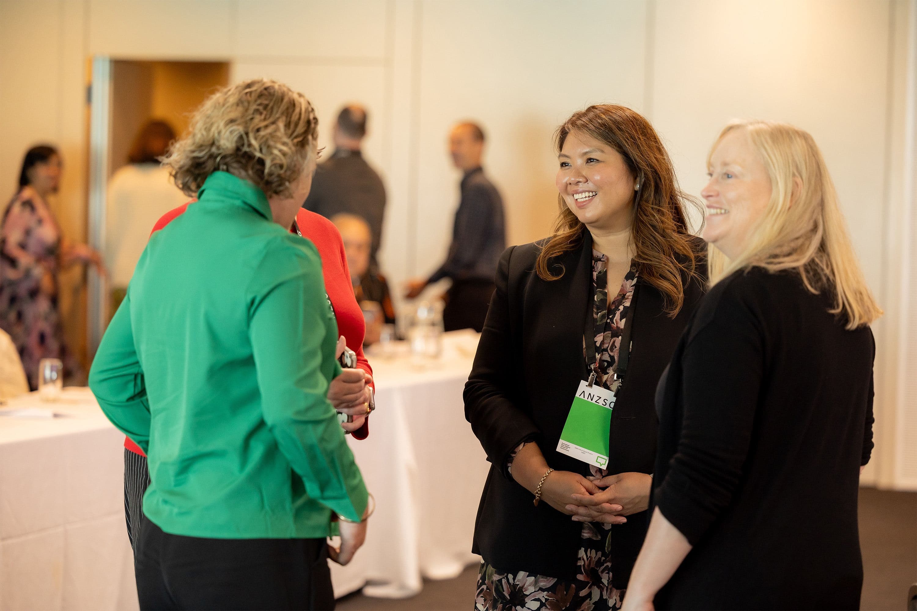 Three women networking at an ANZSC conference, smiling and conversing in a professional event setting.