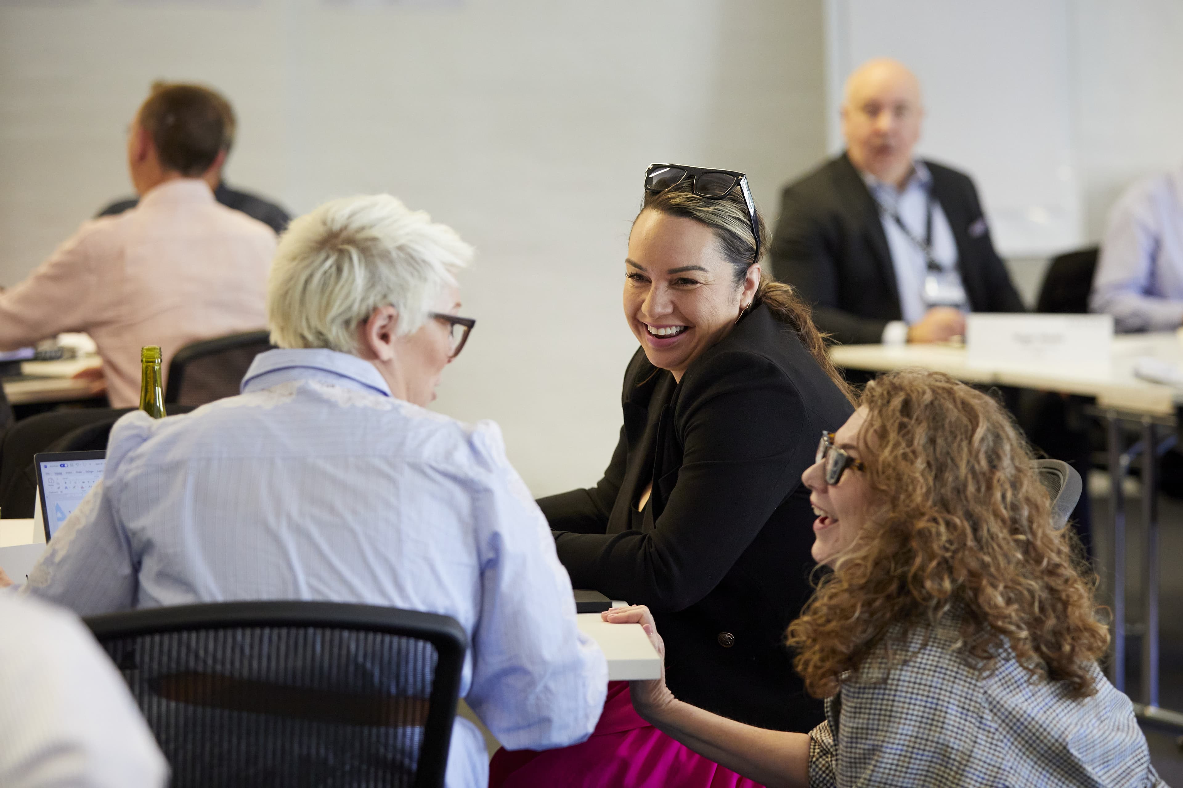 Three colleagues laughing and chatting around a conference table during a casual office meeting.