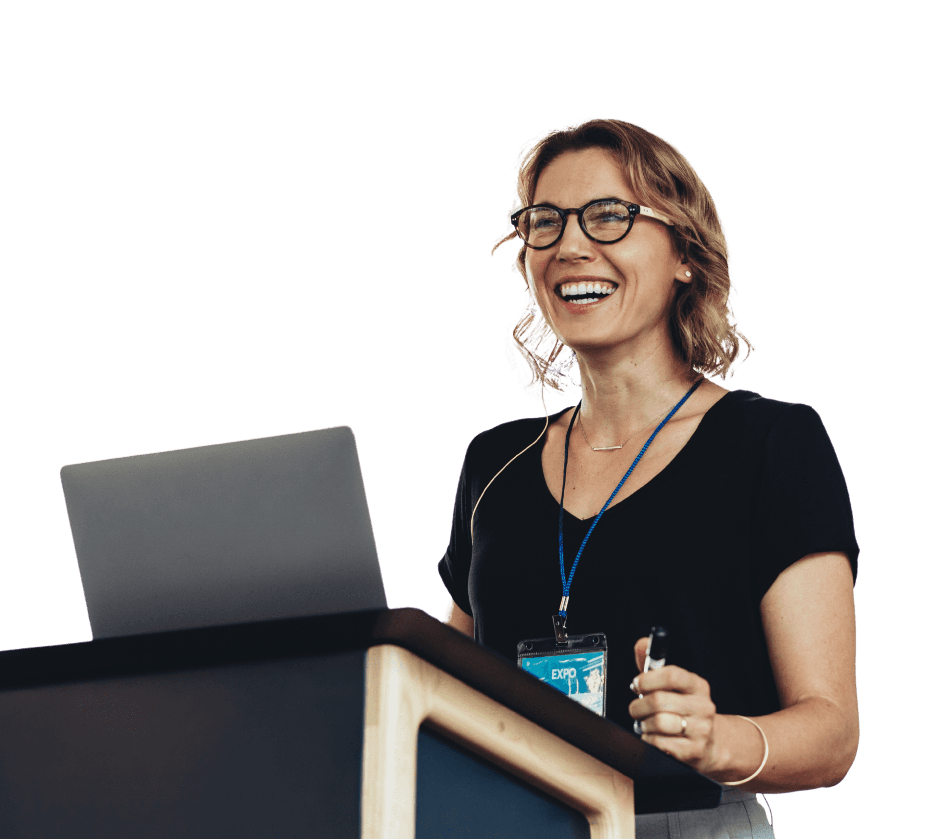 Smiling woman with glasses and a conference badge presenting at a podium with a laptop, wearing a black top.