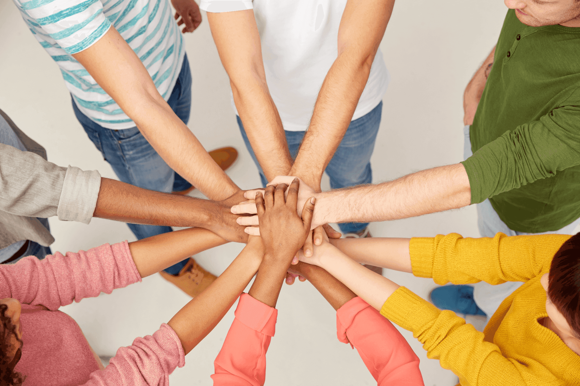A diverse group of people standing in a circle, each extending a hand to form a stack in the center, symbolizing unity and teamwork.