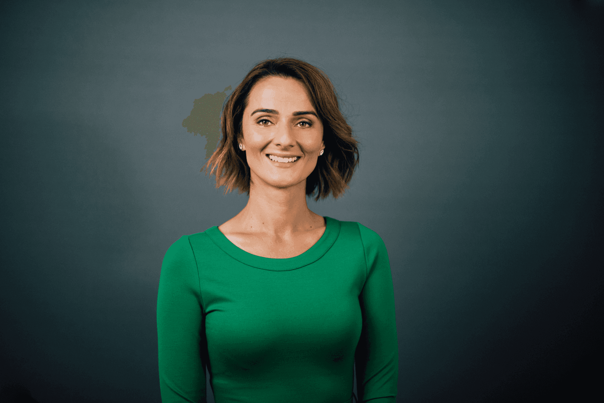 Smiling woman with short brown hair in a green top against a dark gray background.