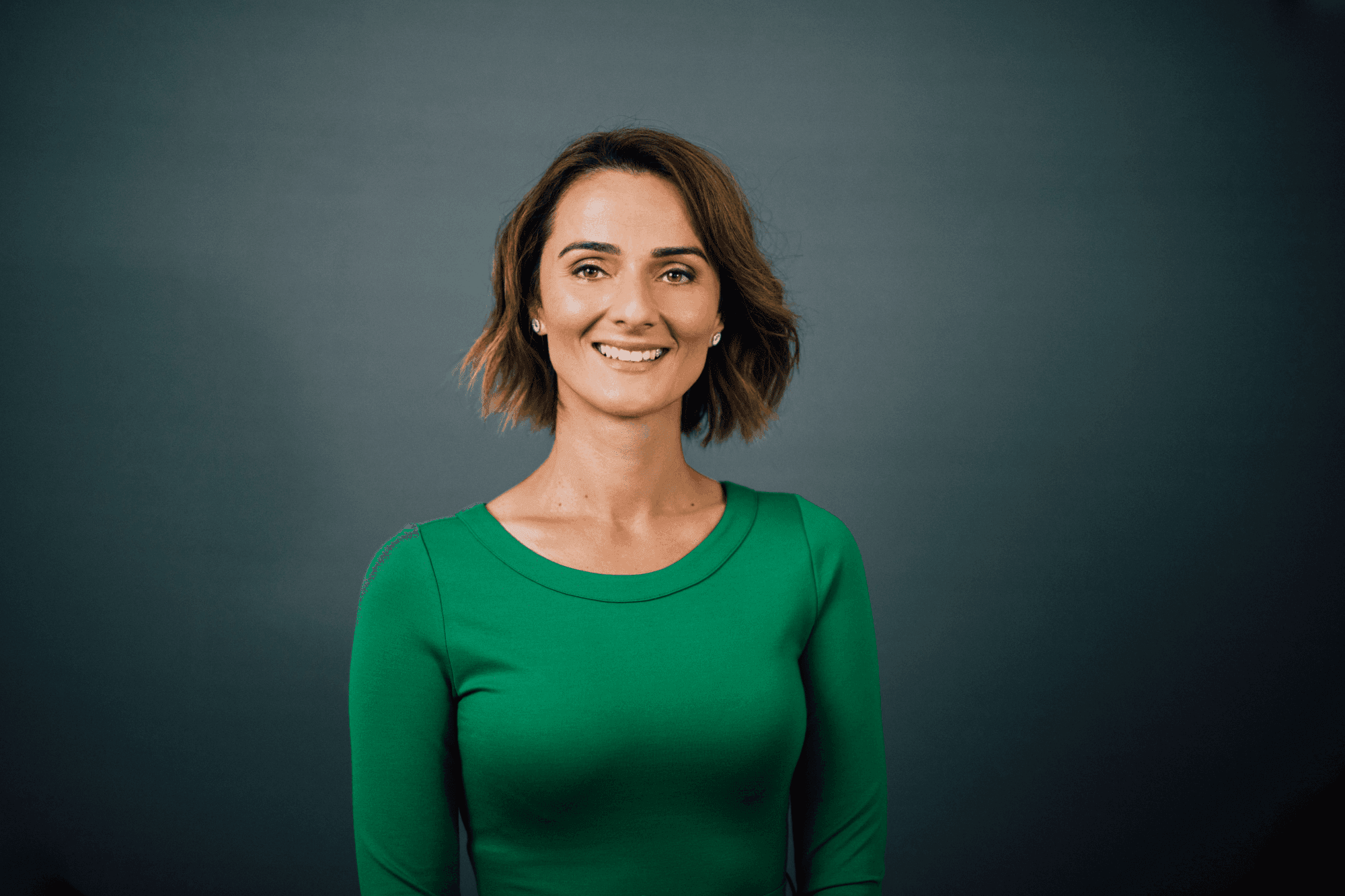 Smiling woman with short brown hair in a green top against a dark gray background.