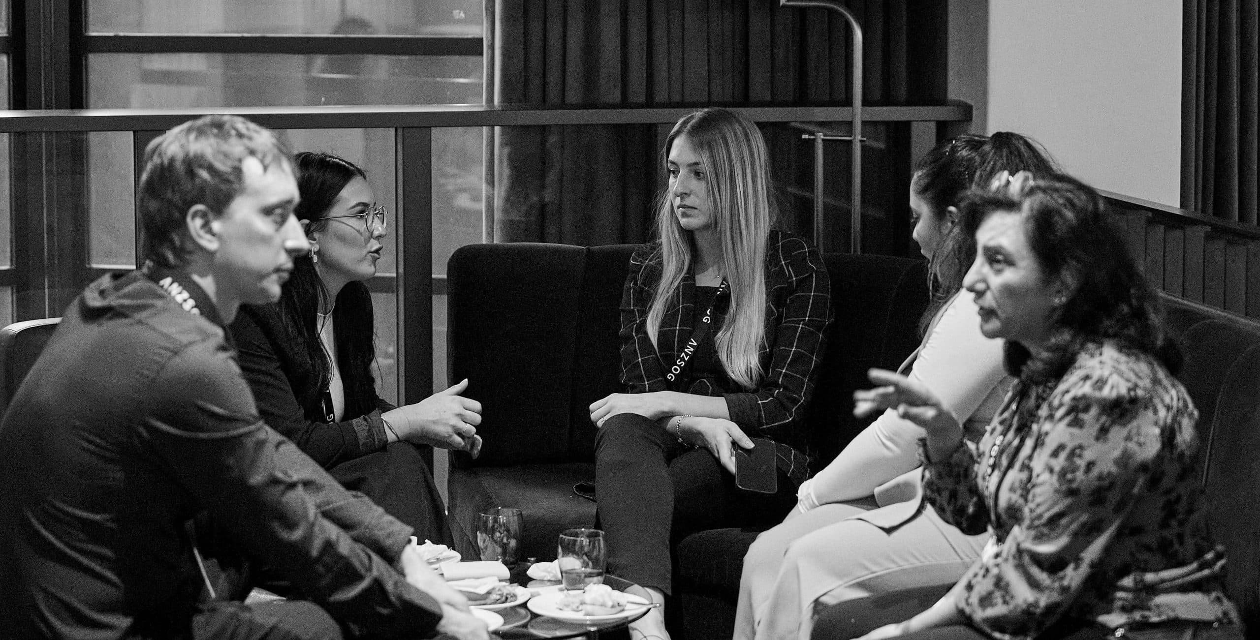 Five people sitting in a semi-circle having a conversation in a casual meeting or networking setting, black and white photo.