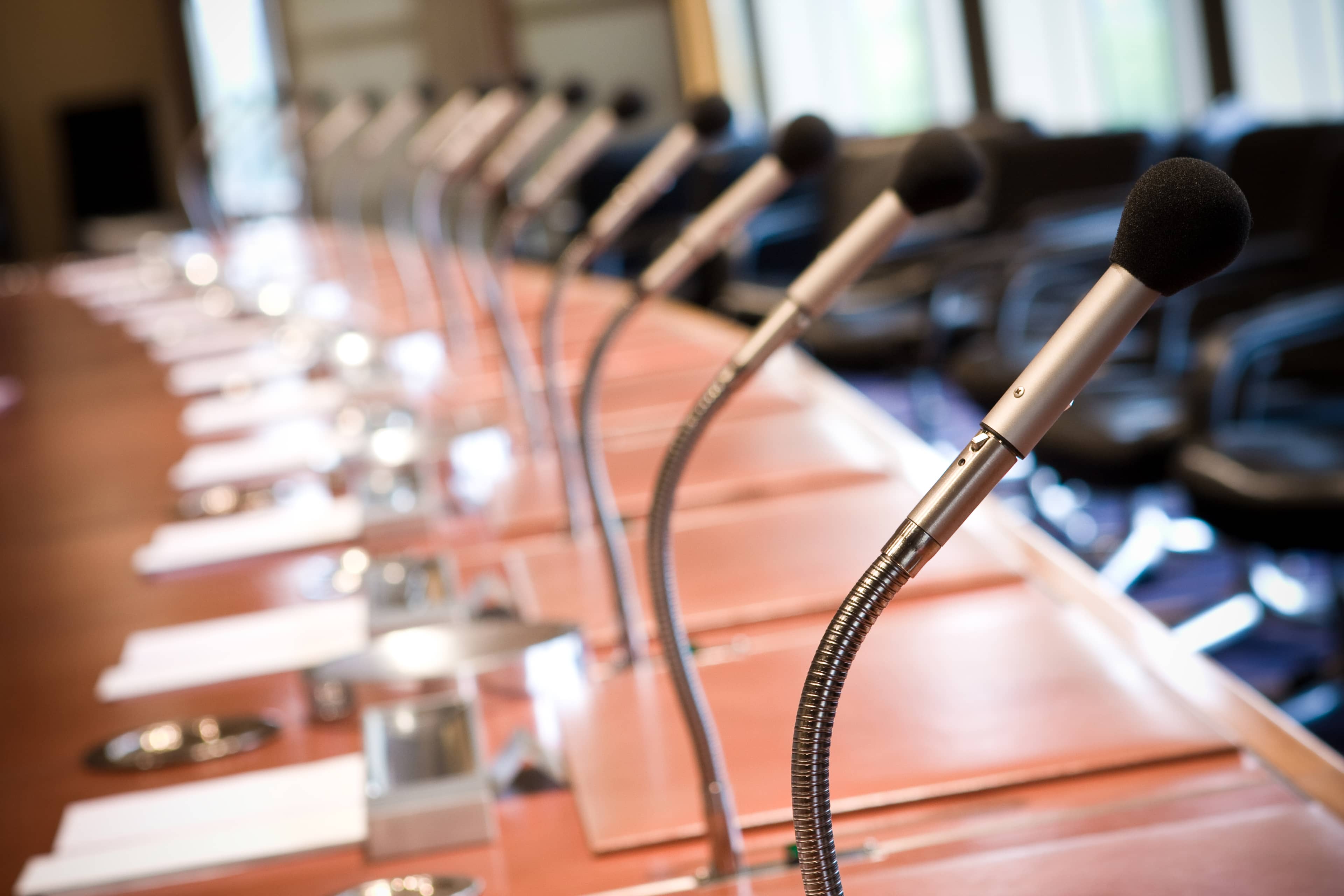 Conference room with a long table, equipped with microphones and neatly arranged notepads and pens, suggesting a meeting setup.