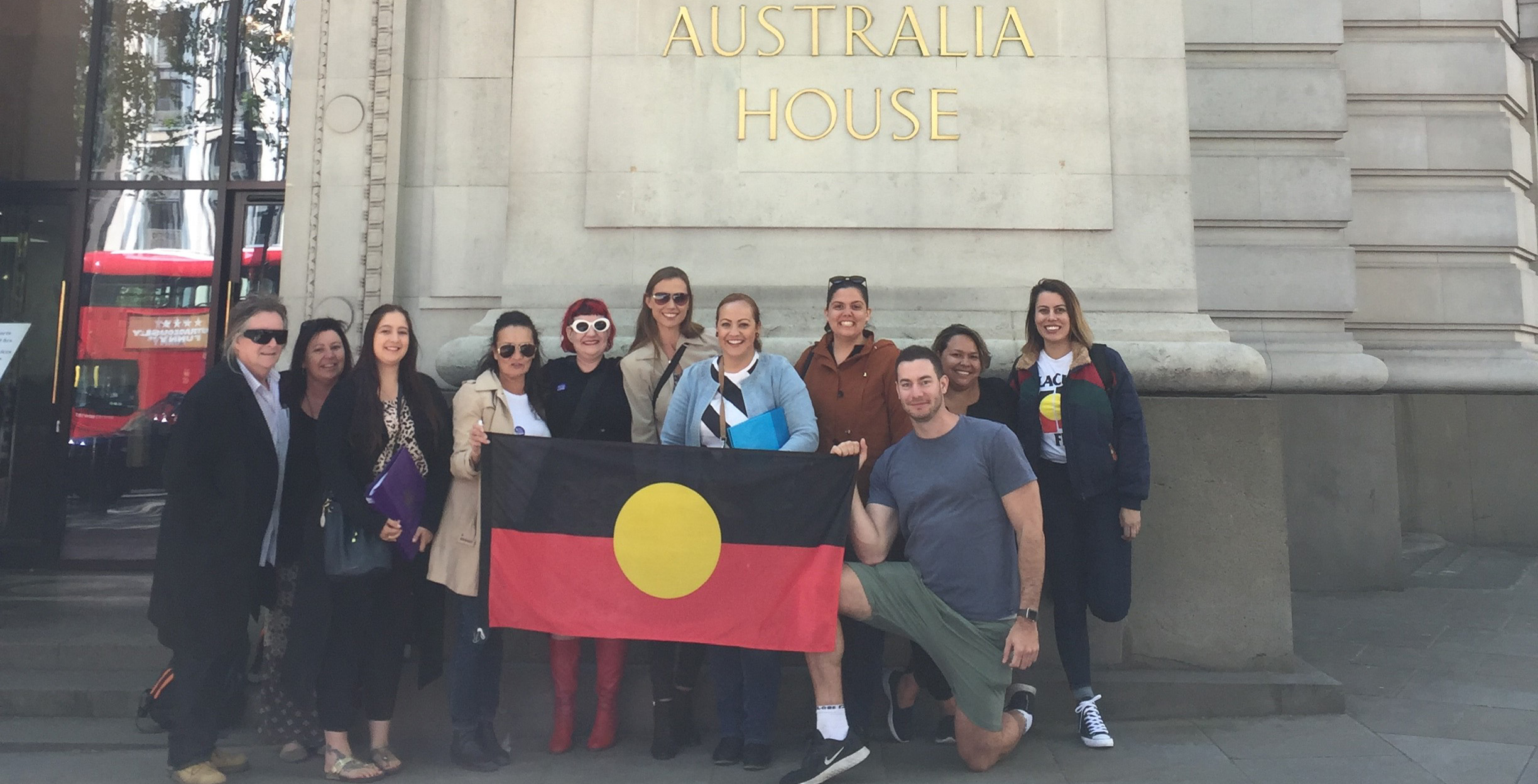 Image of people holding Aboriginal flag outside Australia house