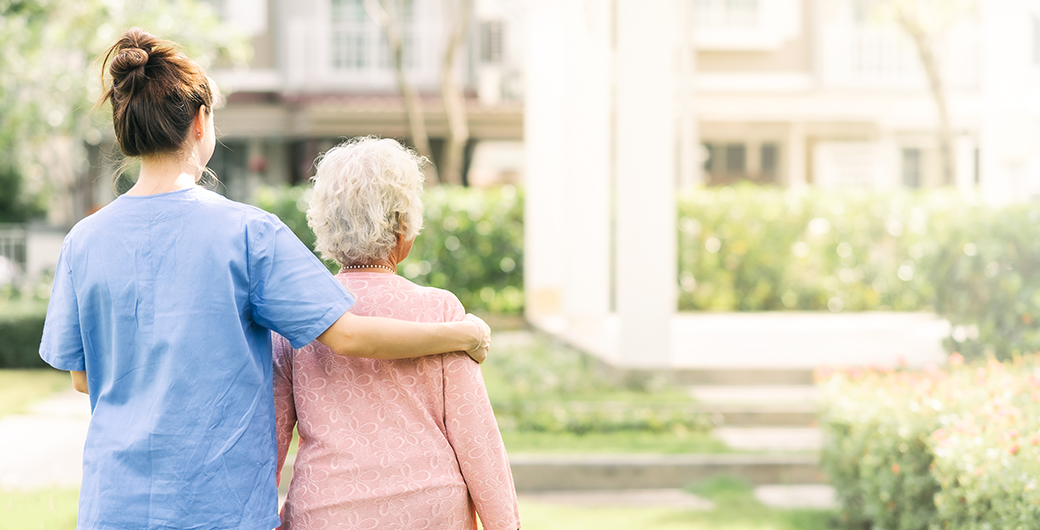 Image of frontline nurse walking with elderly woman outdoors