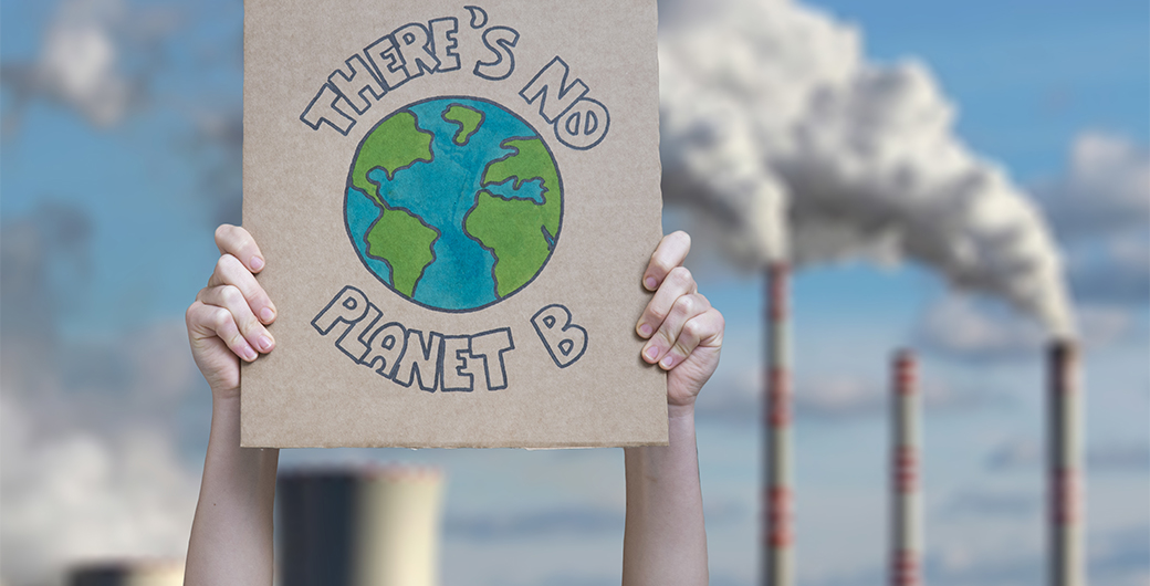 a kid holding a placard 'there is no planet B' wth factories in the background.